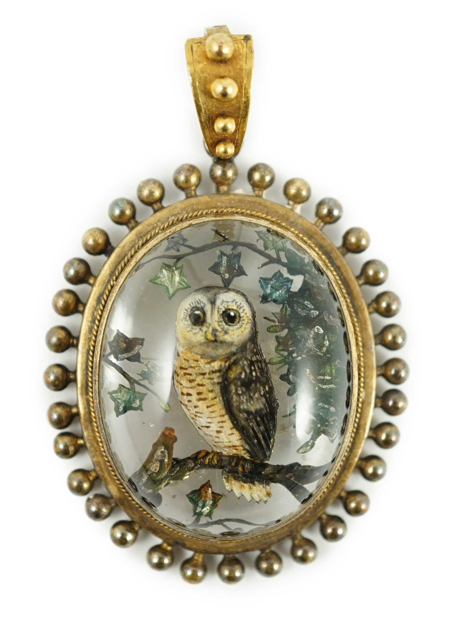 A Victorian yellow metal mounted Essex crystal oval pendant, depicting an owl upon a branch, amid foliage